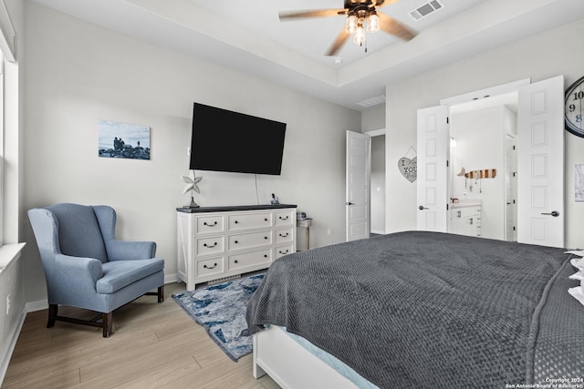 bedroom featuring light wood-style flooring, a ceiling fan, baseboards, a tray ceiling, and visible vents