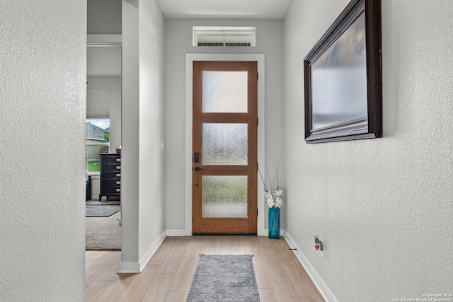 doorway to outside featuring a textured wall, a wealth of natural light, baseboards, and light wood-style floors