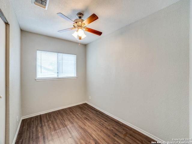 empty room with baseboards, a ceiling fan, dark wood finished floors, and visible vents