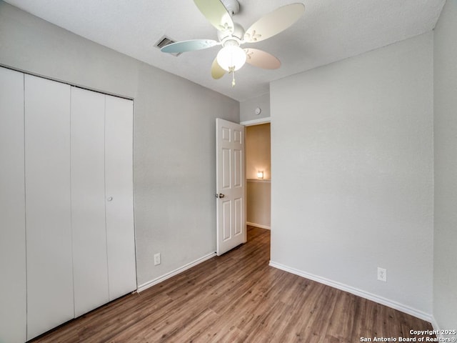 unfurnished bedroom with baseboards, visible vents, wood finished floors, and a closet
