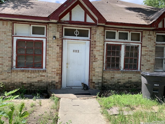 entrance to property featuring brick siding and a shingled roof