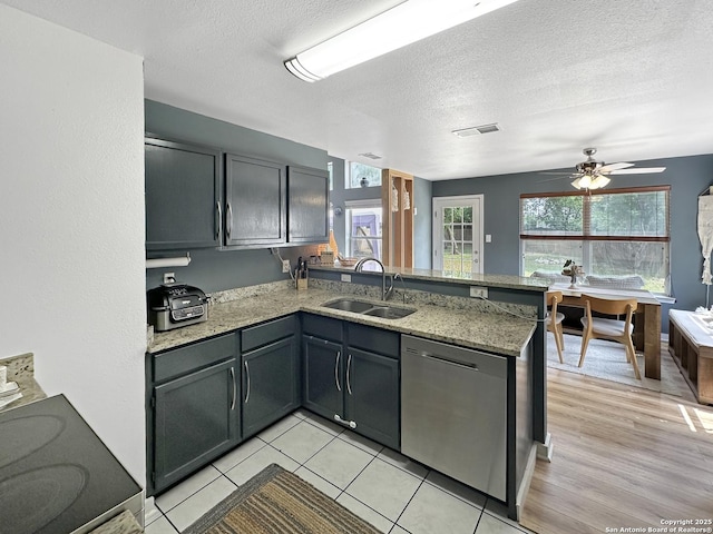 kitchen with a sink, a textured ceiling, a peninsula, stainless steel dishwasher, and visible vents