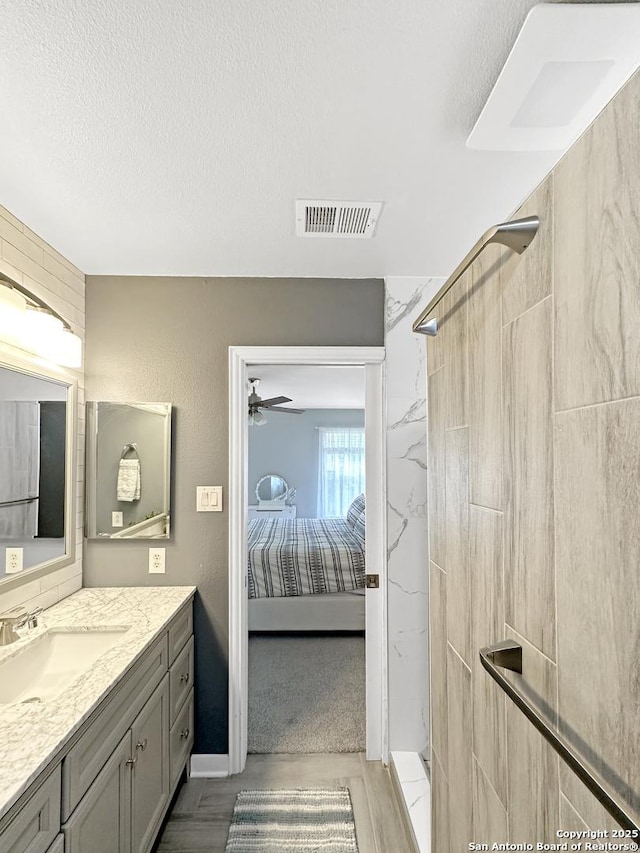 ensuite bathroom with a tile shower, ensuite bath, vanity, a textured ceiling, and visible vents