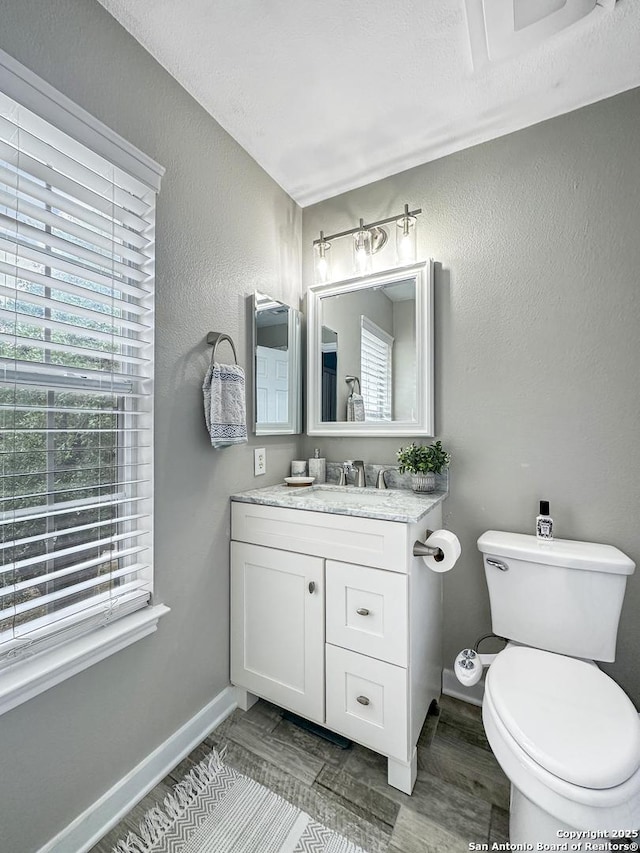 half bath featuring toilet, baseboards, a textured wall, and vanity