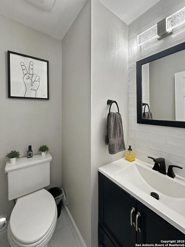 half bathroom featuring vanity, tile patterned flooring, toilet, baseboards, and tasteful backsplash