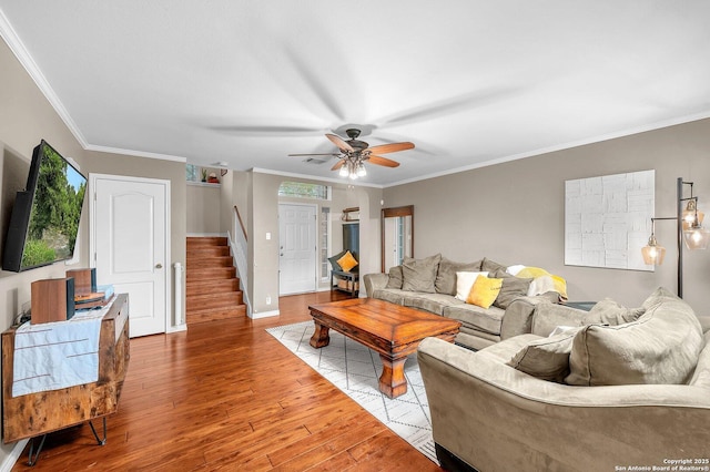 living room with a ceiling fan, wood finished floors, stairway, baseboards, and ornamental molding