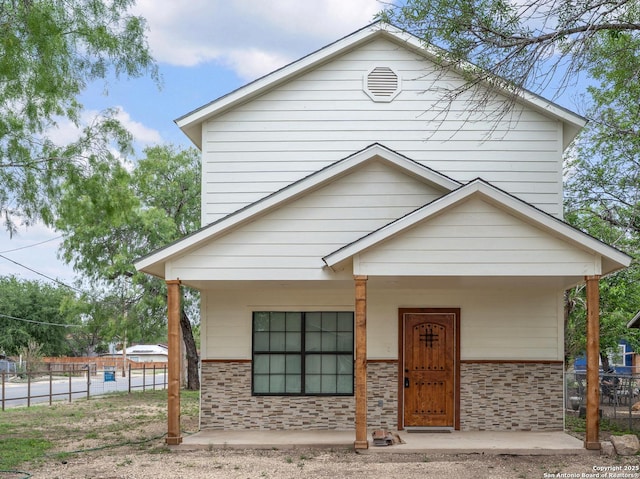 view of front facade featuring fence, a porch, and stone siding