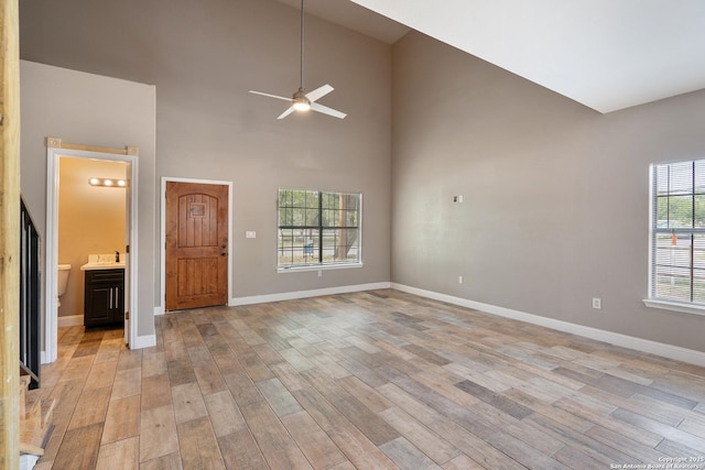 unfurnished living room with baseboards, a ceiling fan, light wood-type flooring, and a towering ceiling