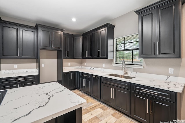 kitchen with a sink, dark cabinets, light wood-style floors, and light stone countertops