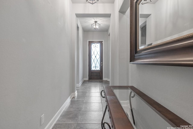 doorway to outside with baseboards, tile patterned floors, and a chandelier