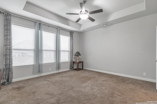 empty room featuring a raised ceiling, carpet floors, a ceiling fan, baseboards, and visible vents
