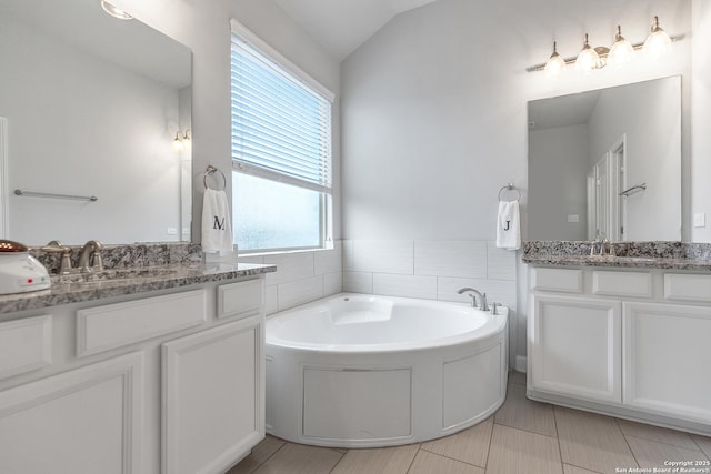bathroom with tile walls, two vanities, a sink, and a garden tub