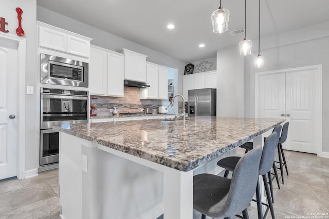 kitchen with visible vents, under cabinet range hood, a sink, stone counters, and appliances with stainless steel finishes