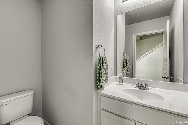 bathroom with vanity, a textured wall, toilet, and a textured ceiling
