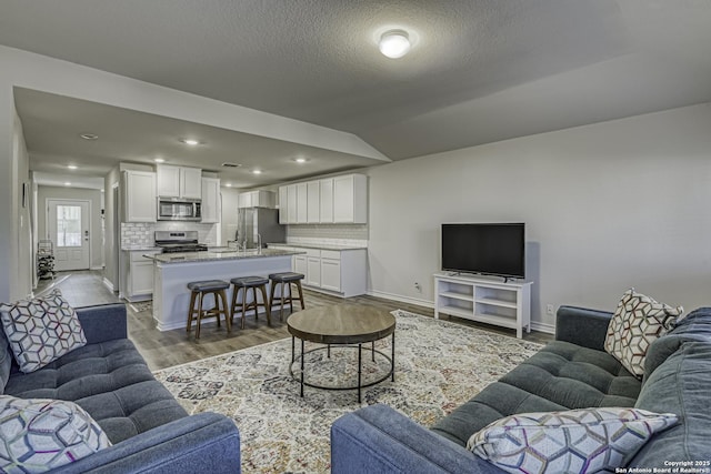 living area featuring recessed lighting, a textured ceiling, baseboards, and wood finished floors
