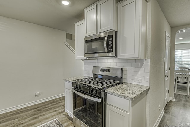 kitchen featuring baseboards, appliances with stainless steel finishes, decorative backsplash, and light wood-style flooring