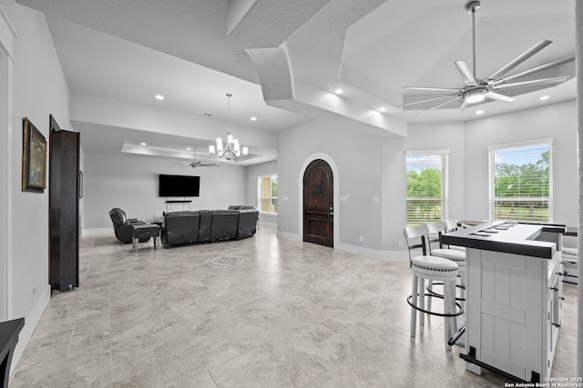 living area featuring baseboards, ceiling fan with notable chandelier, recessed lighting, and a raised ceiling