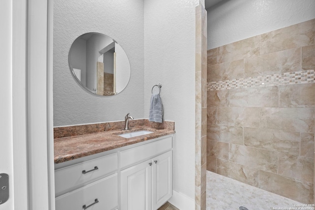 bathroom with a walk in shower, a textured wall, and vanity