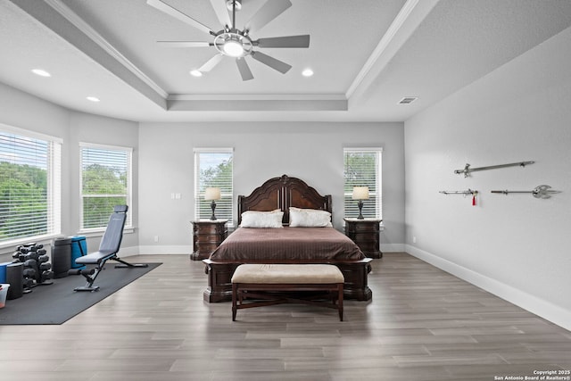 bedroom with ornamental molding, multiple windows, wood finished floors, and a raised ceiling