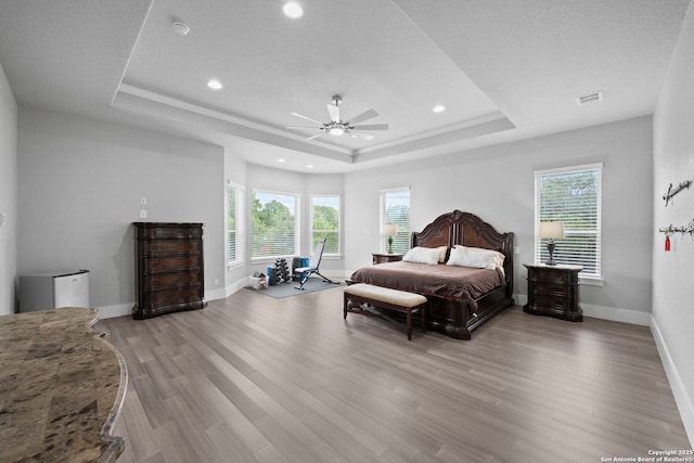bedroom with recessed lighting, multiple windows, a tray ceiling, and light wood-type flooring
