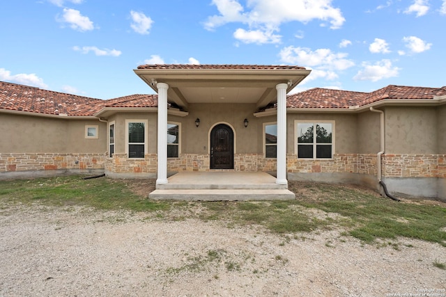 back of property with stucco siding, stone siding, and a tile roof