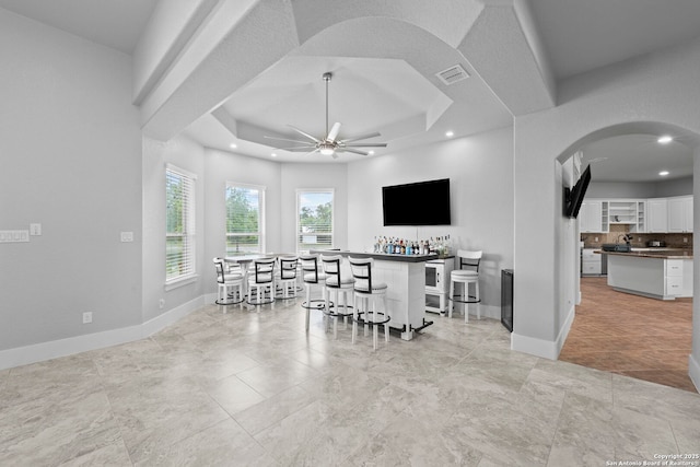 interior space with a ceiling fan, visible vents, arched walkways, a dry bar, and baseboards