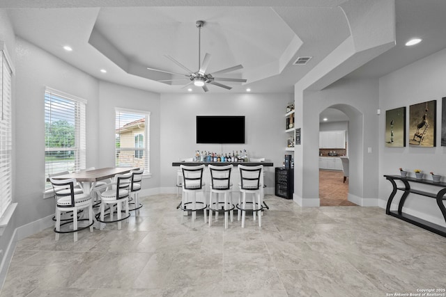 dining space featuring a ceiling fan, visible vents, arched walkways, a bar, and a tray ceiling