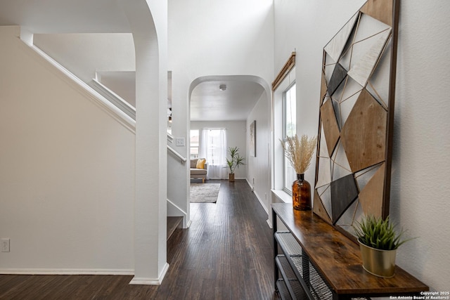 hall with stairway, arched walkways, baseboards, and wood finished floors
