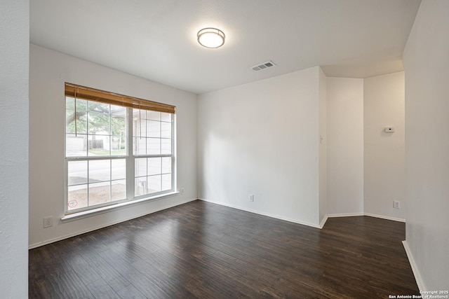 empty room featuring dark wood-style flooring, baseboards, and visible vents