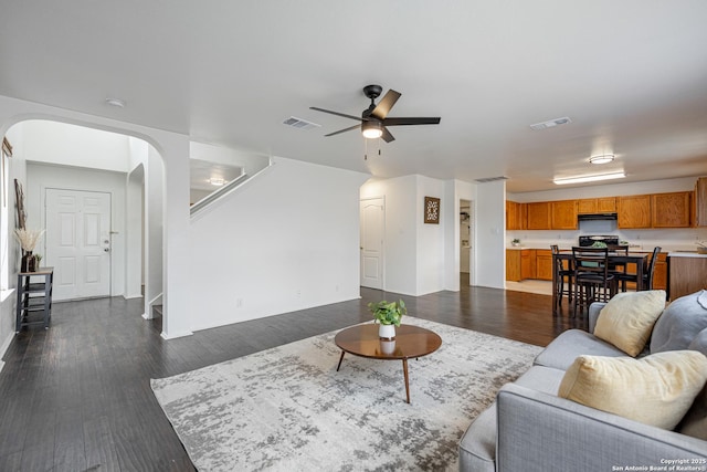living room featuring arched walkways, a ceiling fan, visible vents, and dark wood-type flooring