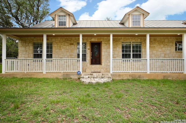 view of front of house with covered porch, a front yard, metal roof, and stone siding