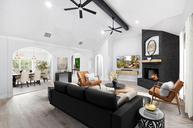 living area with ceiling fan, visible vents, arched walkways, wood finished floors, and beamed ceiling