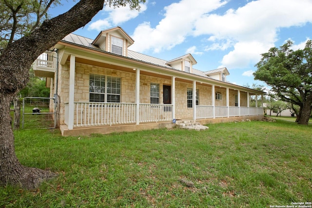 view of front of property with covered porch, metal roof, stone siding, and a front lawn