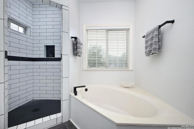 bathroom featuring a healthy amount of sunlight, tiled shower, and a bath