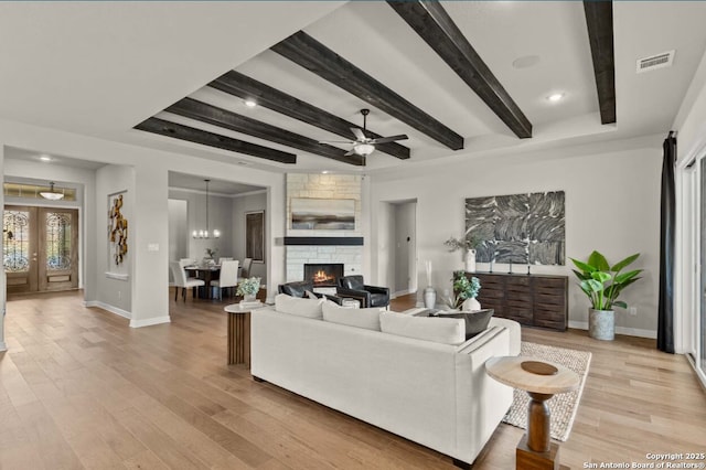 living area with light wood-style floors, a stone fireplace, baseboards, beamed ceiling, and visible vents