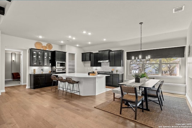 kitchen featuring dark cabinetry, a notable chandelier, tasteful backsplash, and visible vents