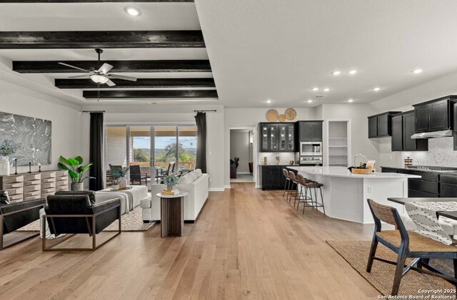 living room with light wood-type flooring, a ceiling fan, recessed lighting, and beamed ceiling