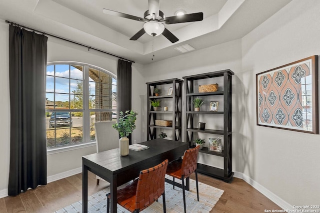 office featuring baseboards, a ceiling fan, a raised ceiling, and wood finished floors