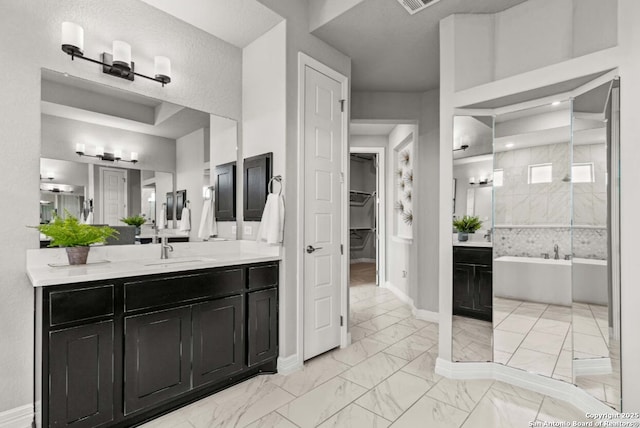 full bathroom featuring a walk in closet, vanity, marble finish floor, baseboards, and a bath