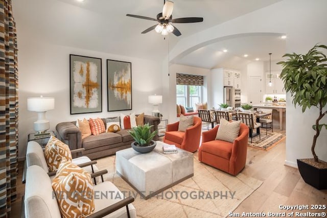 living area with light wood-style floors, arched walkways, a ceiling fan, recessed lighting, and vaulted ceiling