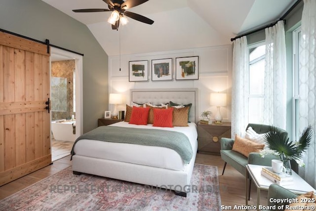 bedroom with ceiling fan, vaulted ceiling, a barn door, wood finished floors, and connected bathroom