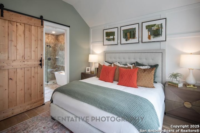 bedroom with ensuite bathroom, a barn door, lofted ceiling, and wood finished floors