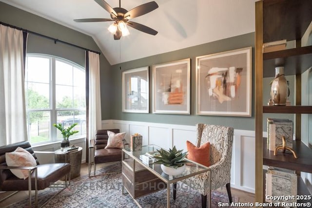 living area with a ceiling fan, wood finished floors, a wainscoted wall, lofted ceiling, and a decorative wall