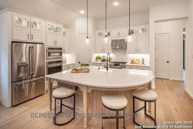 kitchen with white cabinets, tasteful backsplash, range hood, light wood-type flooring, and premium appliances