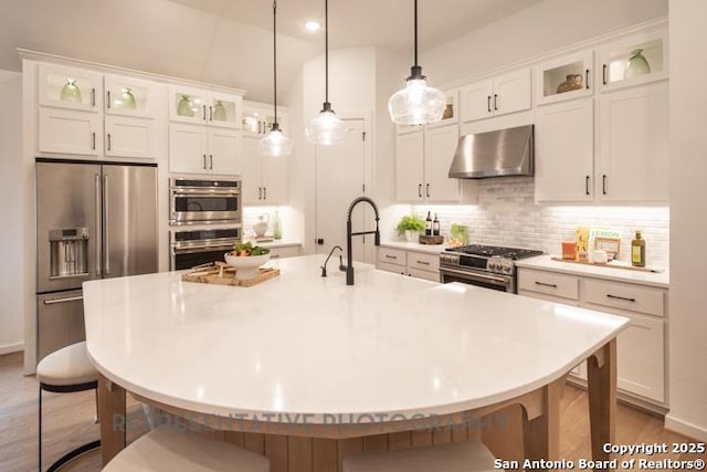 kitchen featuring white cabinets, high quality appliances, a kitchen breakfast bar, decorative backsplash, and range hood