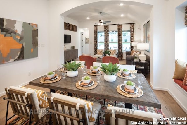 dining space with ceiling fan, arched walkways, vaulted ceiling, wood finished floors, and baseboards