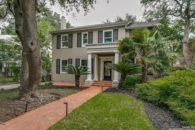 view of front of house featuring a chimney, a front yard, and stucco siding
