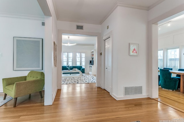 hall featuring visible vents, ornamental molding, and light wood-style flooring