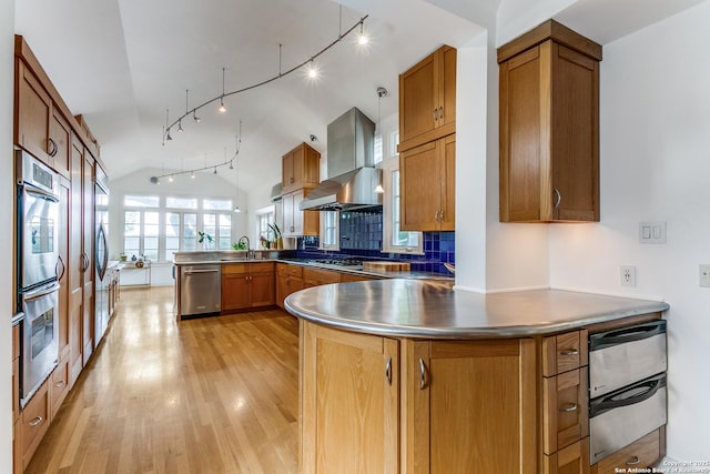 kitchen featuring wall chimney range hood, appliances with stainless steel finishes, light wood finished floors, rail lighting, and a peninsula