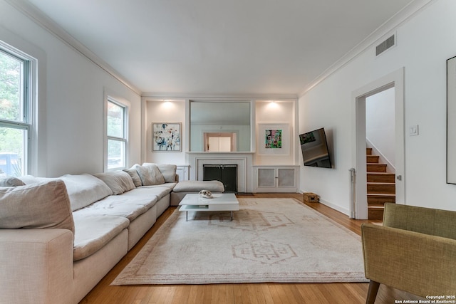 living room with a fireplace, stairs, wood finished floors, visible vents, and ornamental molding